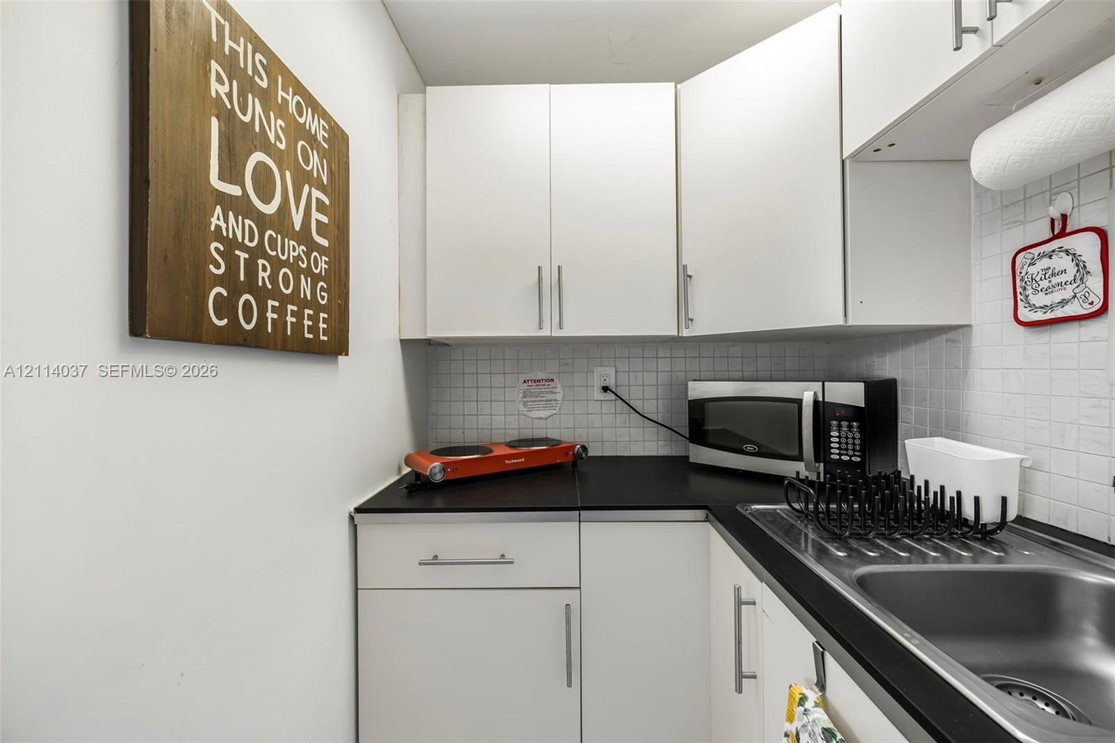 Kitchenette featuring white cabinetry, black countertops, stainless steel sink, and white tiled backsplash