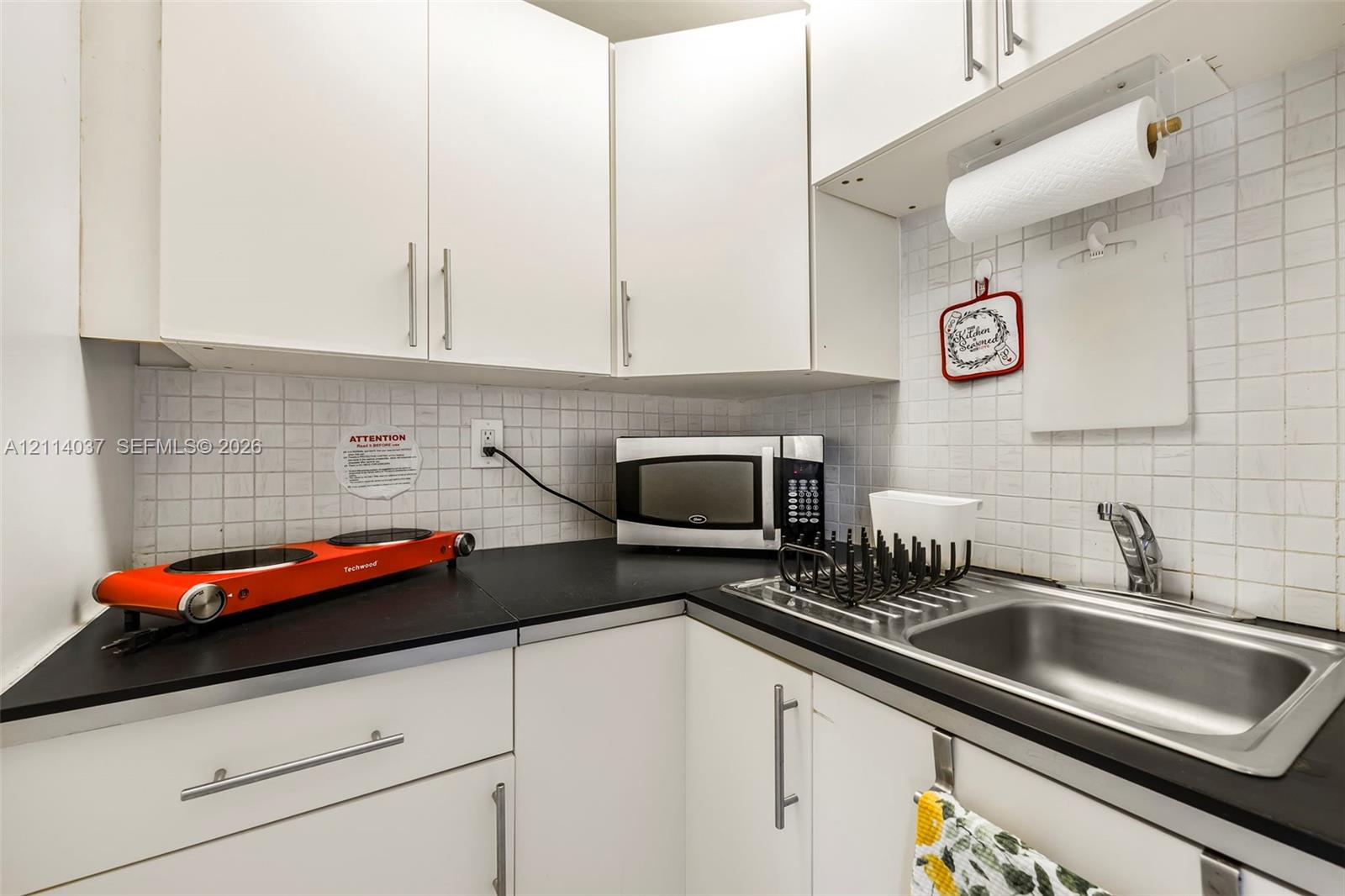 Kitchenette featuring white cabinetry, black countertops, stainless steel sink with a high-arch faucet, and a tiled backsplash