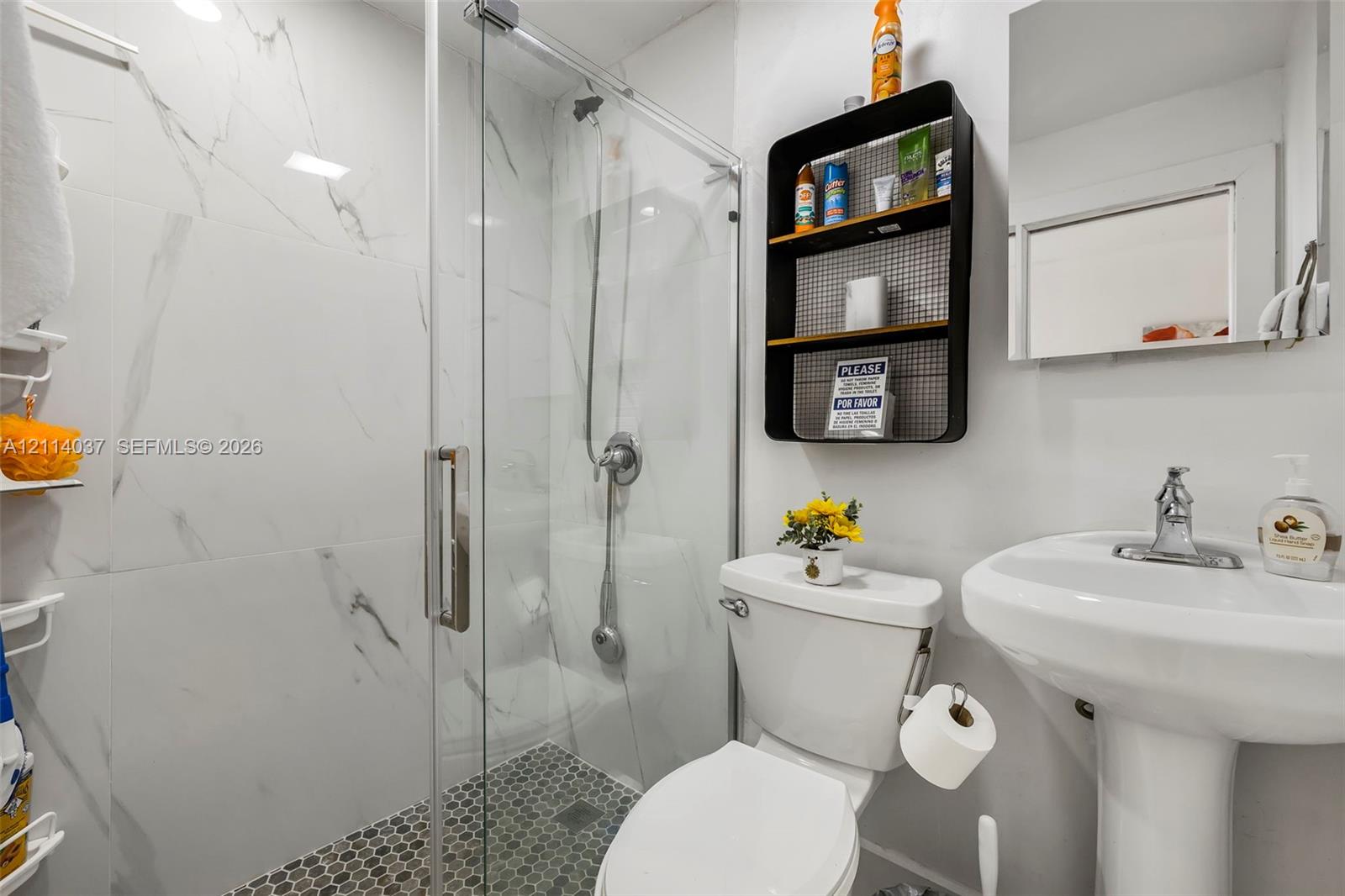 Walk-in glass shower with floor-to-ceiling large-format stone-finish tiling, hexagonal mosaic tile shower flooring, and pedestal sink