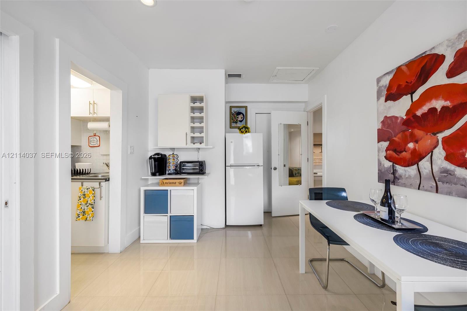 Light-toned tile flooring, white interior cabinetry, and a full-height refrigerator in a neutral-painted space