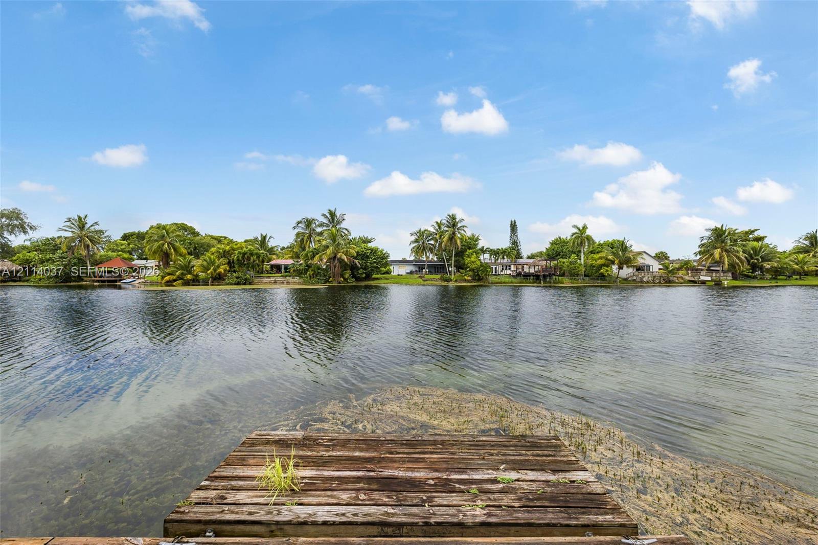 Waterfront property featuring a wooden dock, expansive canal, and lush tropical landscaping
