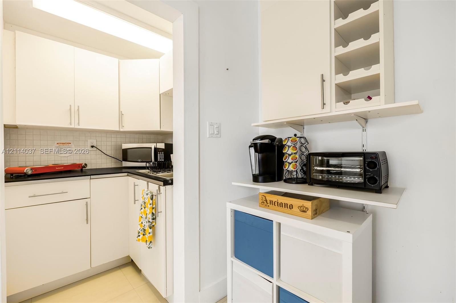 Kitchen featuring white cabinetry, dark countertops, square tile backsplash, and built-in wine storage