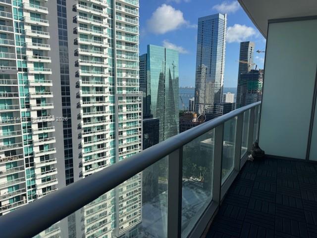 Covered balcony featuring square interlocking floor tiles and a full-height glass railing with a metallic handrail