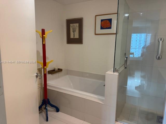 Bathroom featuring a deep-soaking bathtub with tile surround and a separate glass-enclosed shower with installed grab bar