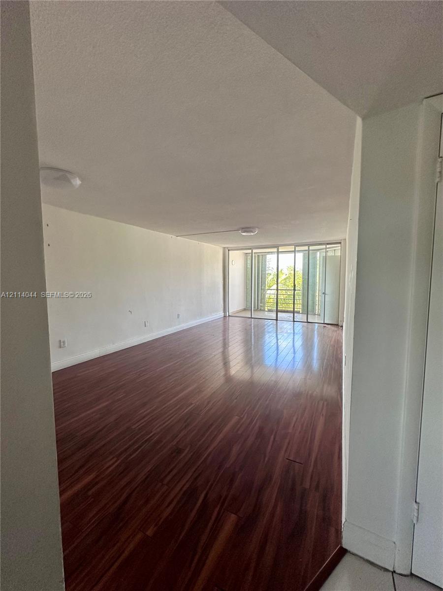 Open interior space featuring wood-finish flooring, ceiling-mounted light fixtures, and floor-to-ceiling glass sliding doors opening to a balcony