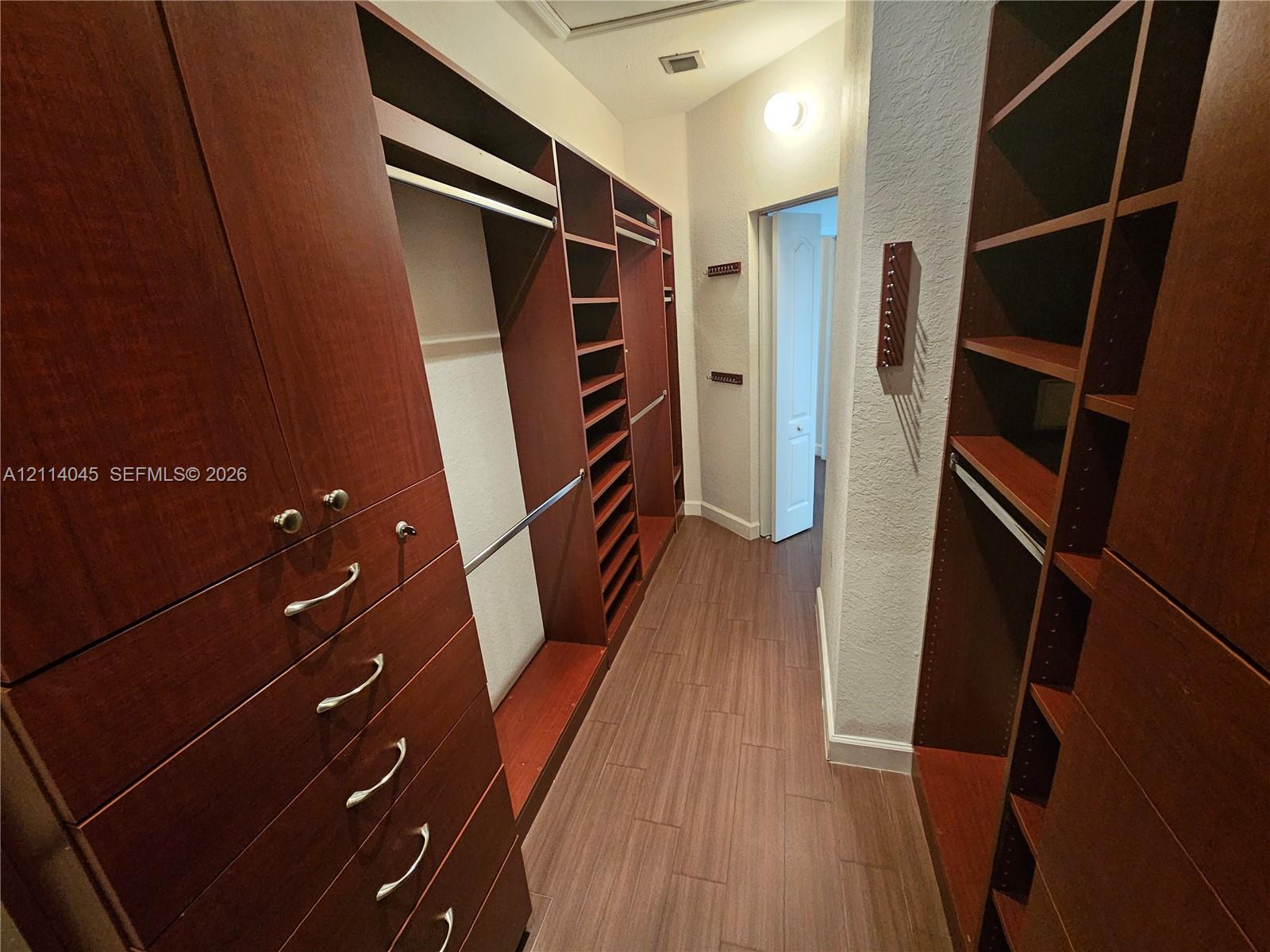 Custom walk-in closet featuring extensive dark wood-finish cabinetry, built-in shelving, integrated hanging rods, and wood-finish flooring