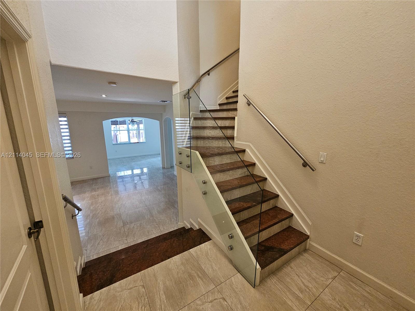 Staircase featuring dark stone treads, glass panel railings, and a metallic handrail, complemented by large-format tile flooring and high ceilings