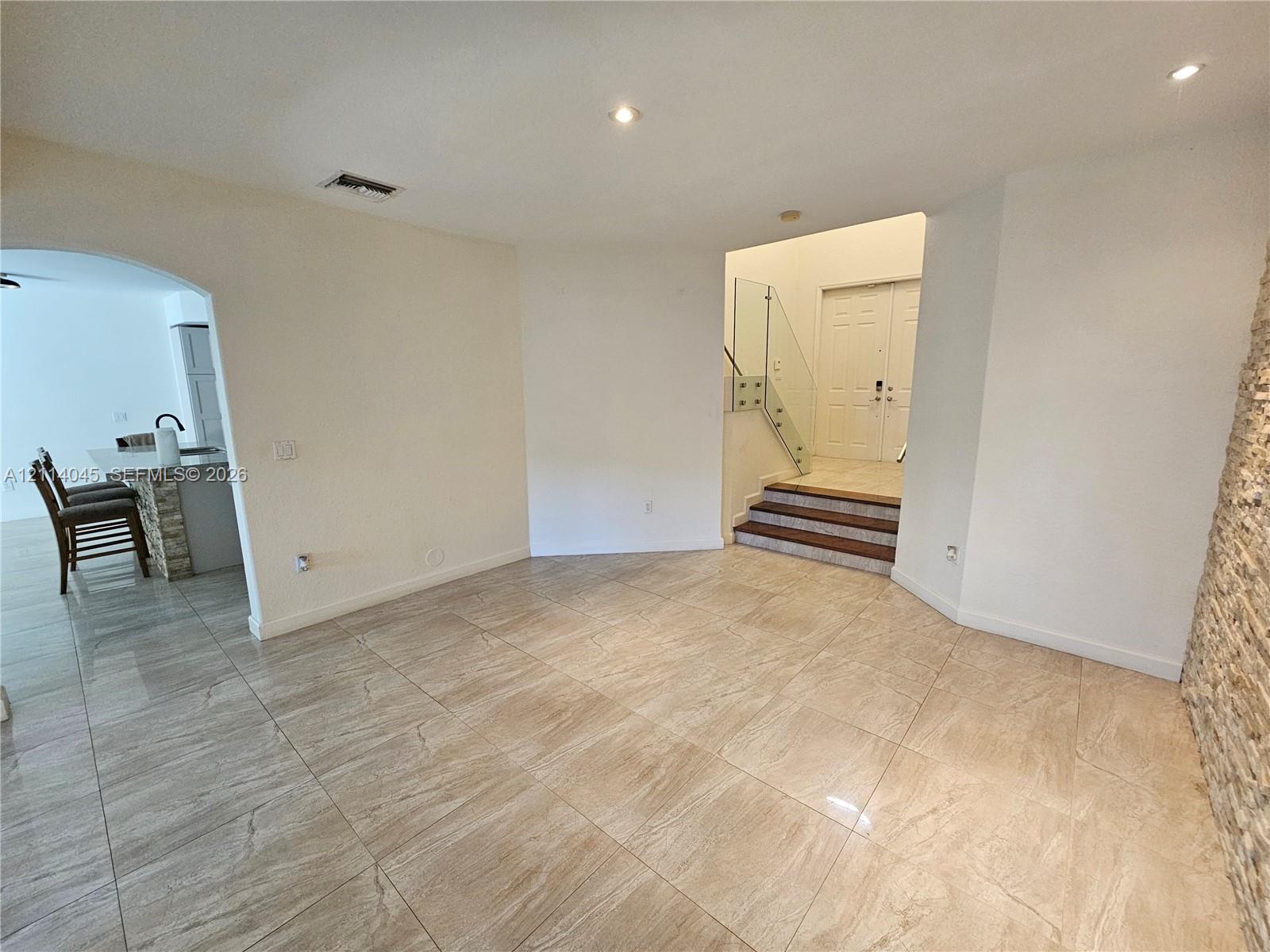 Large-format tile flooring, textured stone accent wall, glass panel staircase railing, recessed lighting, and double-door entry
