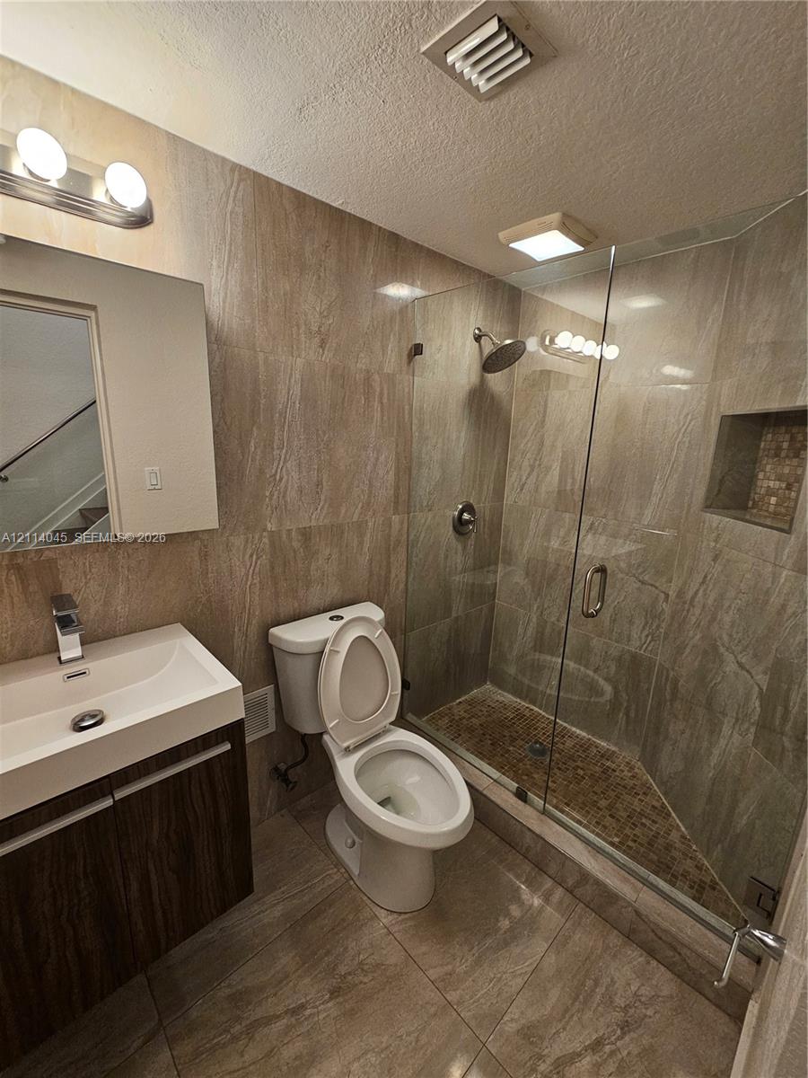 Walk-in shower with a glass enclosure, integrated tile niche, and pebble-style floor tiling, complemented by wood-finish cabinetry, a rectangular vessel sink, and full-wall tile surround