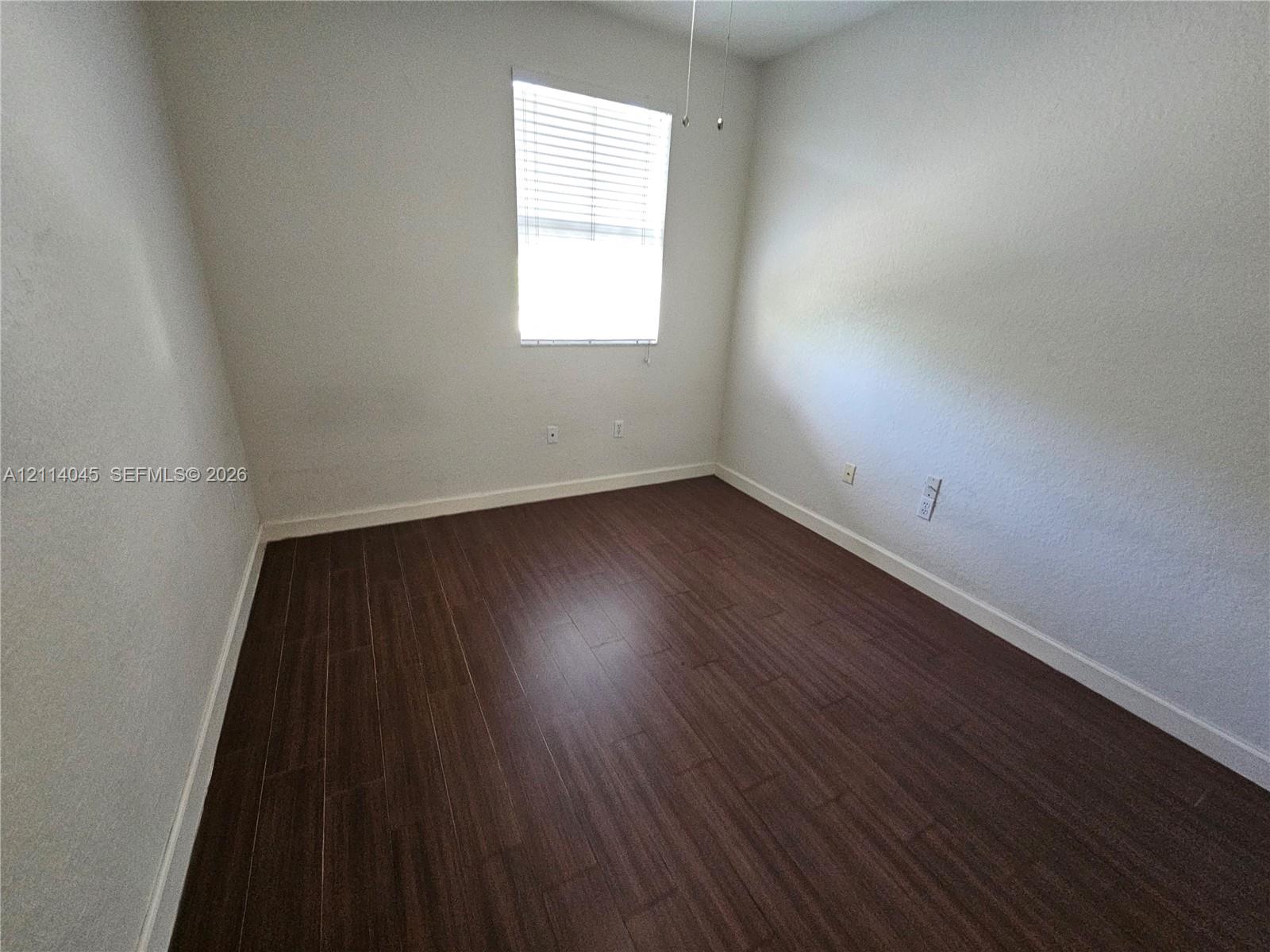 Neutral-toned walls paired with wood-finish flooring and a single-pane window featuring installed blinds