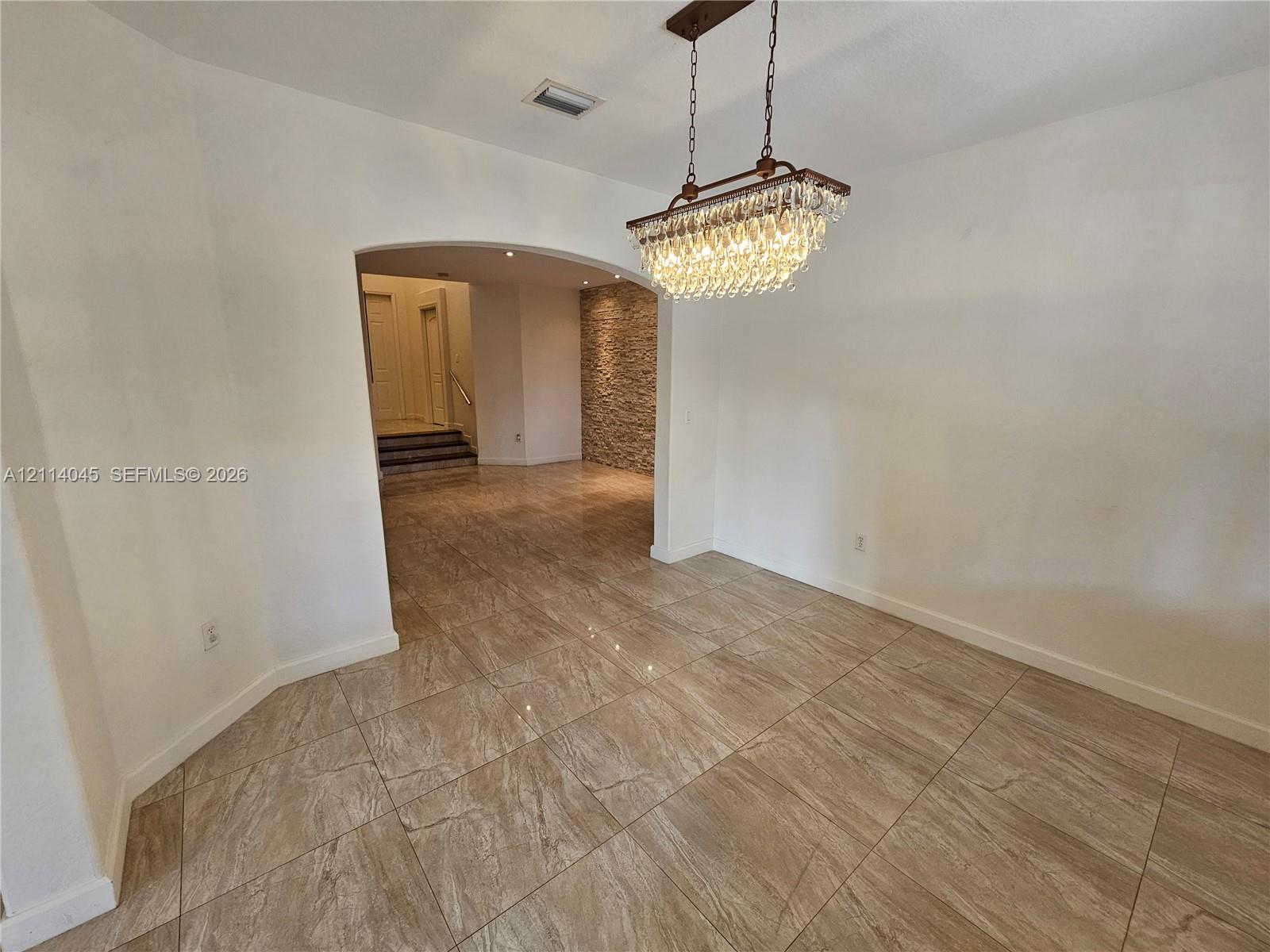 Large-format tile flooring, tiered crystal chandelier, arched entryway, and stone-accented wall finish