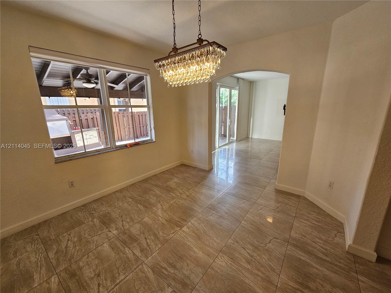 Stone-finish tile flooring, decorative multi-tier crystal chandelier, arched entryway, and double-pane window