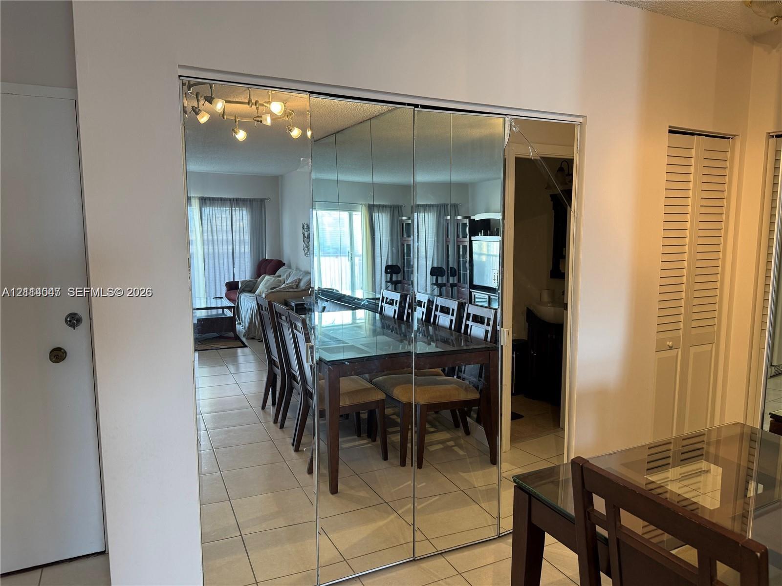 Floor-to-ceiling mirrored panel walls, neutral ceramic tile flooring, and louvered closet doors