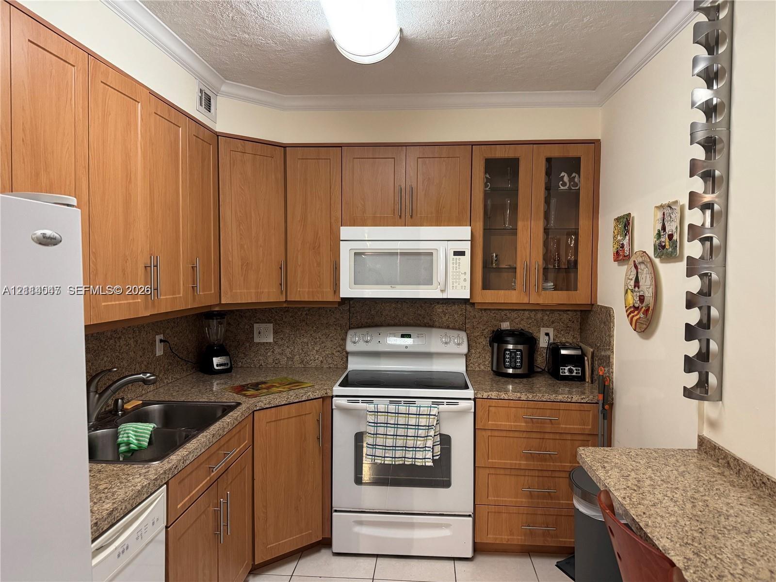 Kitchen featuring wood-finish cabinetry, stone-texture countertops, glass-panel upper cabinet doors, and white appliances including a built-in microwave