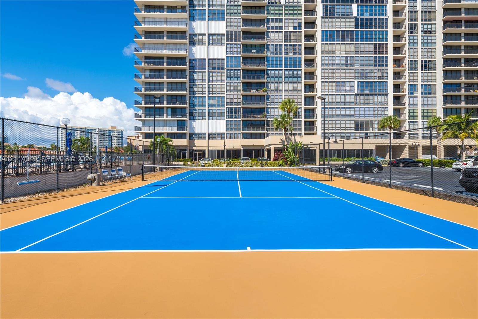 Tennis court featuring a high-contrast blue and tan surface, perimeter chain-link fencing, and exterior light fixtures Tennis court featuring a high-contrast blue and tan surface, perimeter chain-link fencing, and exterior light fixtures