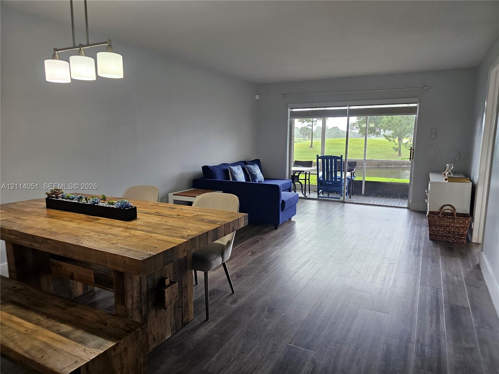 Open-concept interior featuring wood-finish flooring, a three-light linear pendant fixture, and sliding glass doors leading to a screened-in patio Open-concept interior featuring wood-finish flooring, a three-light linear pendant fixture, and sliding glass doors leading to a screened-in patio