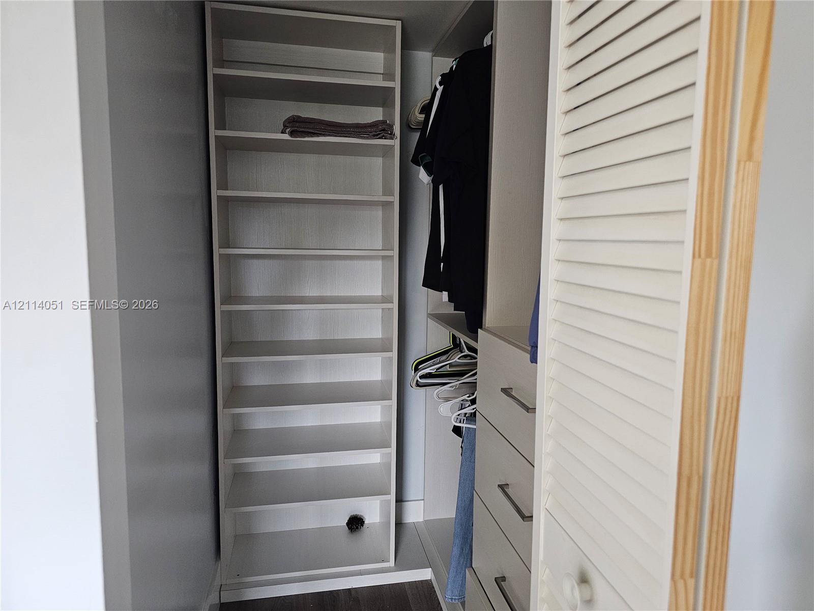 Custom closet organization system featuring vertical shelving, hanging rods, built-in drawers with horizontal bar pulls, and a louvered door