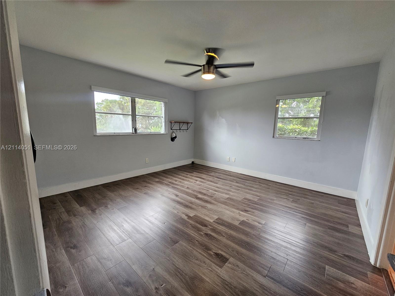 Room featuring wood-finish flooring, two windows with blinds, and a ceiling fan with integrated lighting