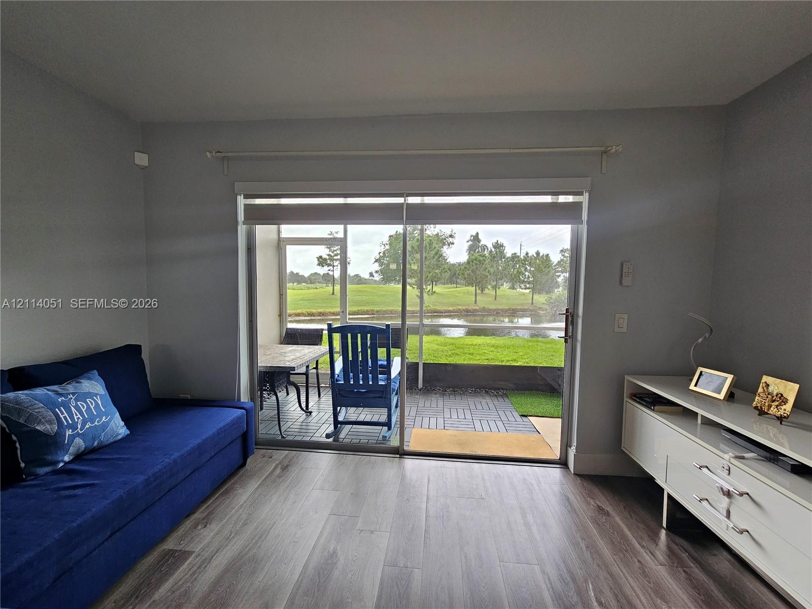 Interior featuring wood-finish flooring, sliding glass doors, and a screen-enclosed patio with interlocking patio tiles overlooking a pond Interior featuring wood-finish flooring, sliding glass doors, and a screen-enclosed patio with interlocking patio tiles overlooking a pond