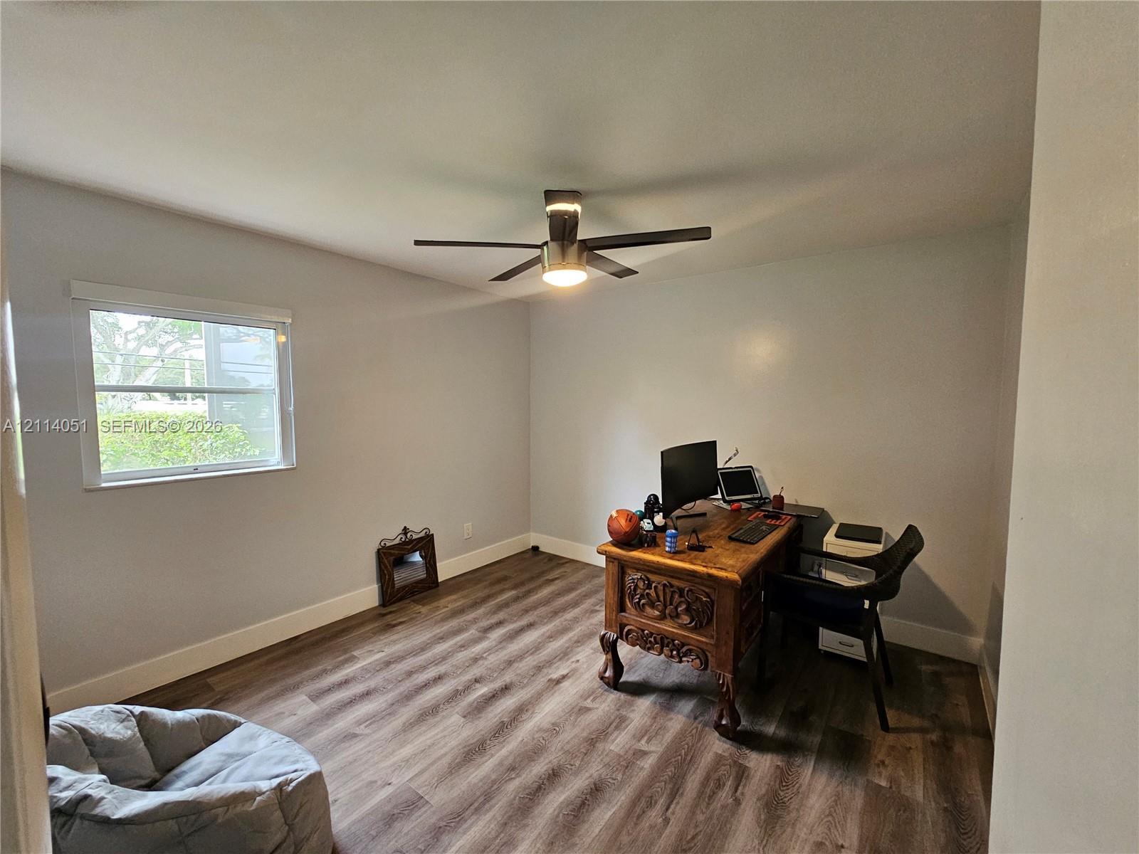Interior room featuring wood-finish flooring, a neutral wall color palette, and a multi-blade ceiling fan with an integrated light fixture