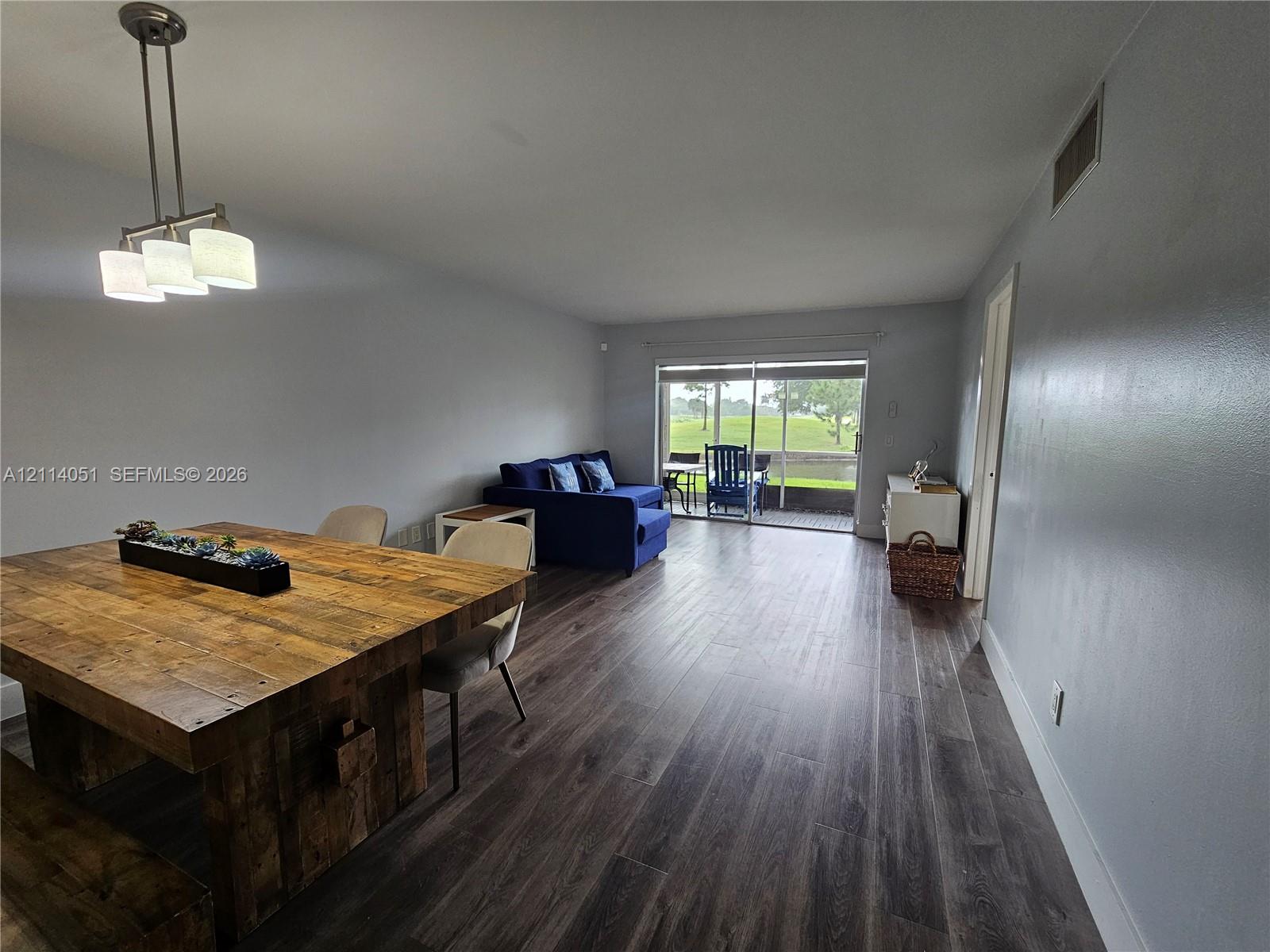 Open-concept space featuring wood-finish flooring, a three-light brushed nickel pendant fixture, and sliding glass doors leading to an exterior screened enclosure Open-concept space featuring wood-finish flooring, a three-light brushed nickel pendant fixture, and sliding glass doors leading to an exterior screened enclosure