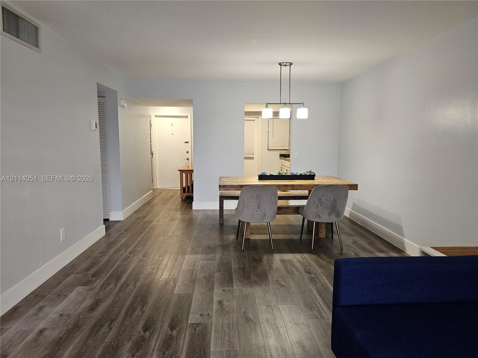 Open-concept interior featuring wood-finish flooring, neutral wall paint, and a modern three-light pendant fixture Open-concept interior featuring wood-finish flooring, neutral wall paint, and a modern three-light pendant fixture