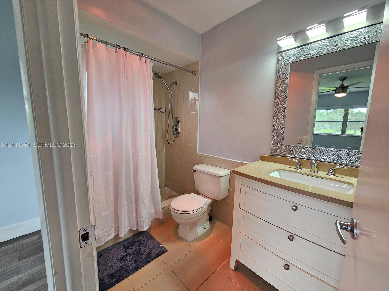 Bathroom featuring a white vanity with three drawers, a neutral-toned countertop with an integrated sink, a framed mirror, a three-bulb light fixture, and a tile-surround shower