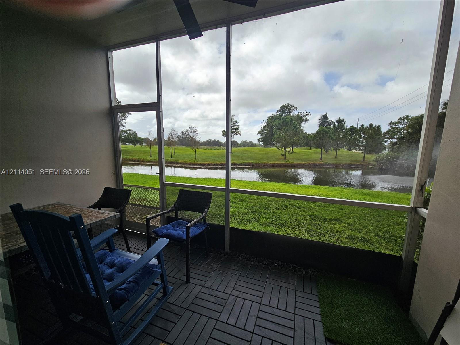 Screen-enclosed porch featuring interlocking deck tiles, ceiling fan, and direct frontage of a pond and green space