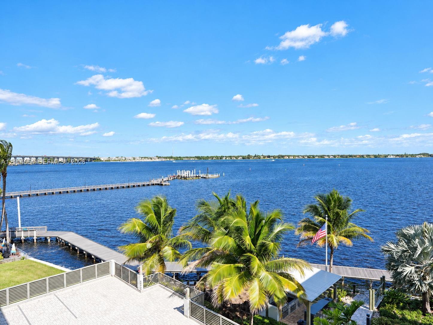 Waterfront terrace featuring stone paving, metal railings, mature palm trees, a dedicated boat dock, and direct access to open water Waterfront terrace featuring stone paving, metal railings, mature palm trees, a dedicated boat dock, and direct access to open water