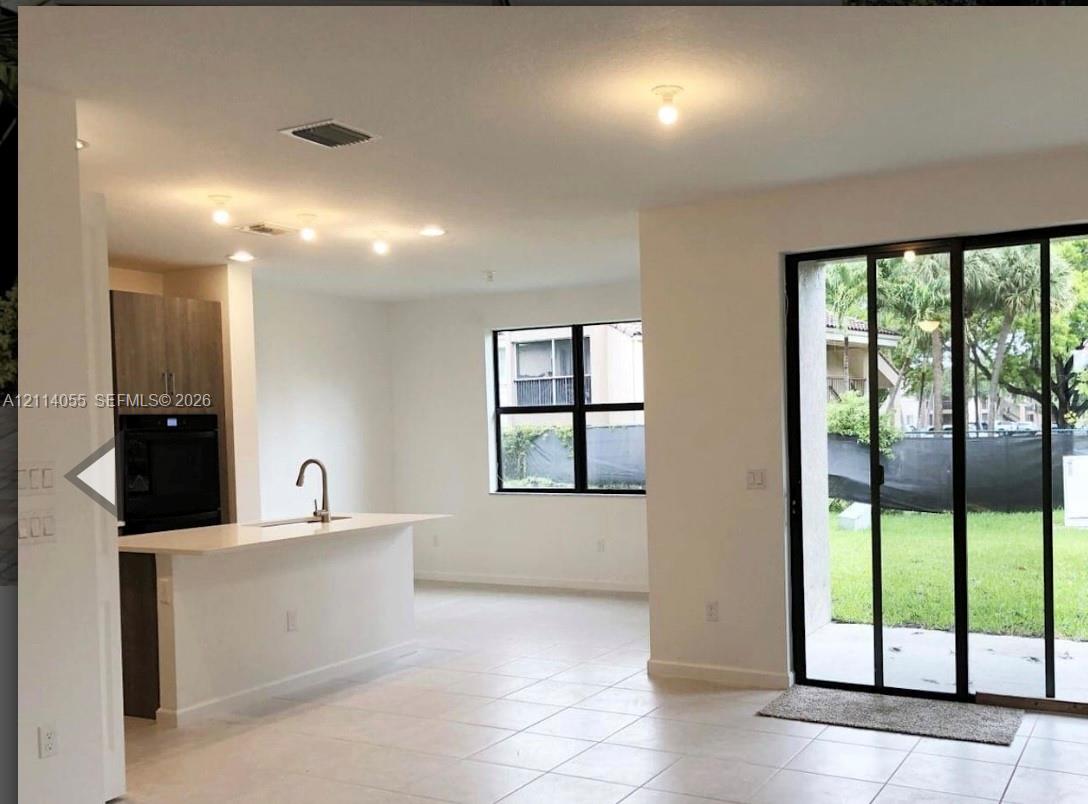 Kitchen island with quartz countertop and undermount sink, built-in wall oven, flat-panel cabinetry, tile flooring, and sliding glass doors Kitchen island with quartz countertop and undermount sink, built-in wall oven, flat-panel cabinetry, tile flooring, and sliding glass doors