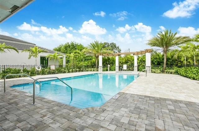 In-ground swimming pool with built-in stairs, surrounded by a stone-paver deck, featuring a pergola structure and mature landscaping In-ground swimming pool with built-in stairs, surrounded by a stone-paver deck, featuring a pergola structure and mature landscaping
