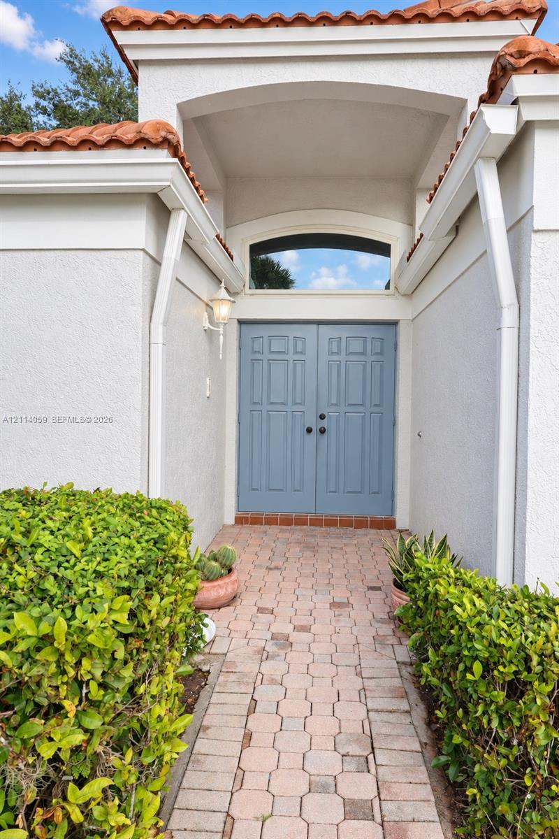 Stucco exterior entryway featuring a terracotta tile roof, arched transom window, dual panel doors, and a decorative wall-mounted lantern