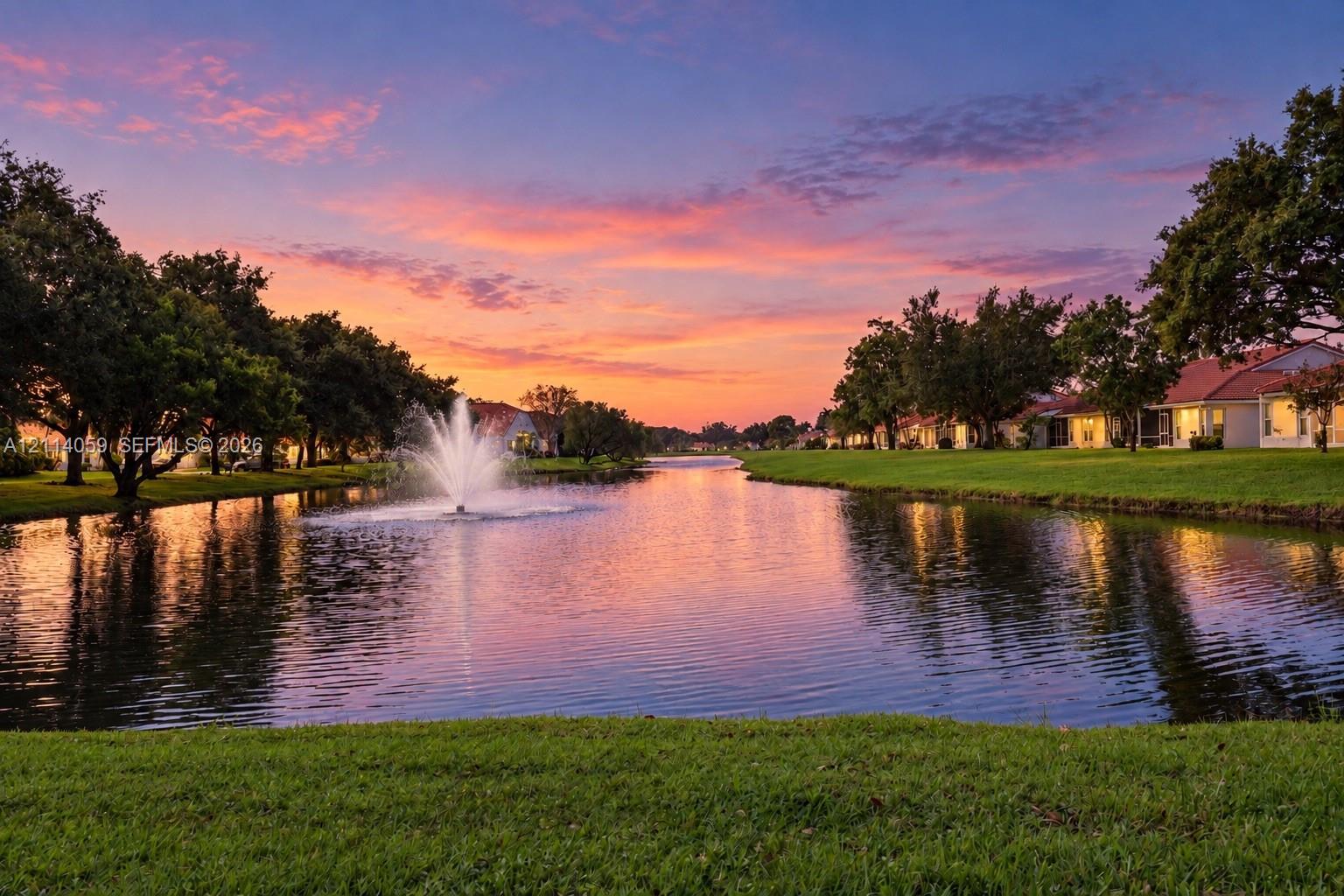 Waterfront pond featuring a central fountain, manicured lawn, and mature trees