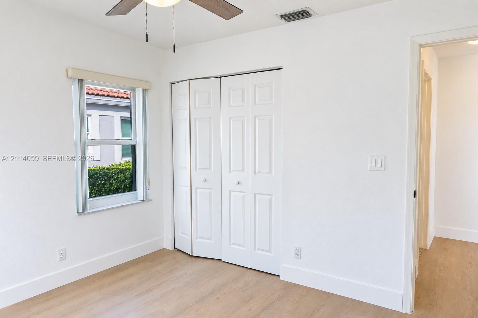 Wood-finish flooring, white paneled bifold closet doors, and a ceiling fan with integrated lighting