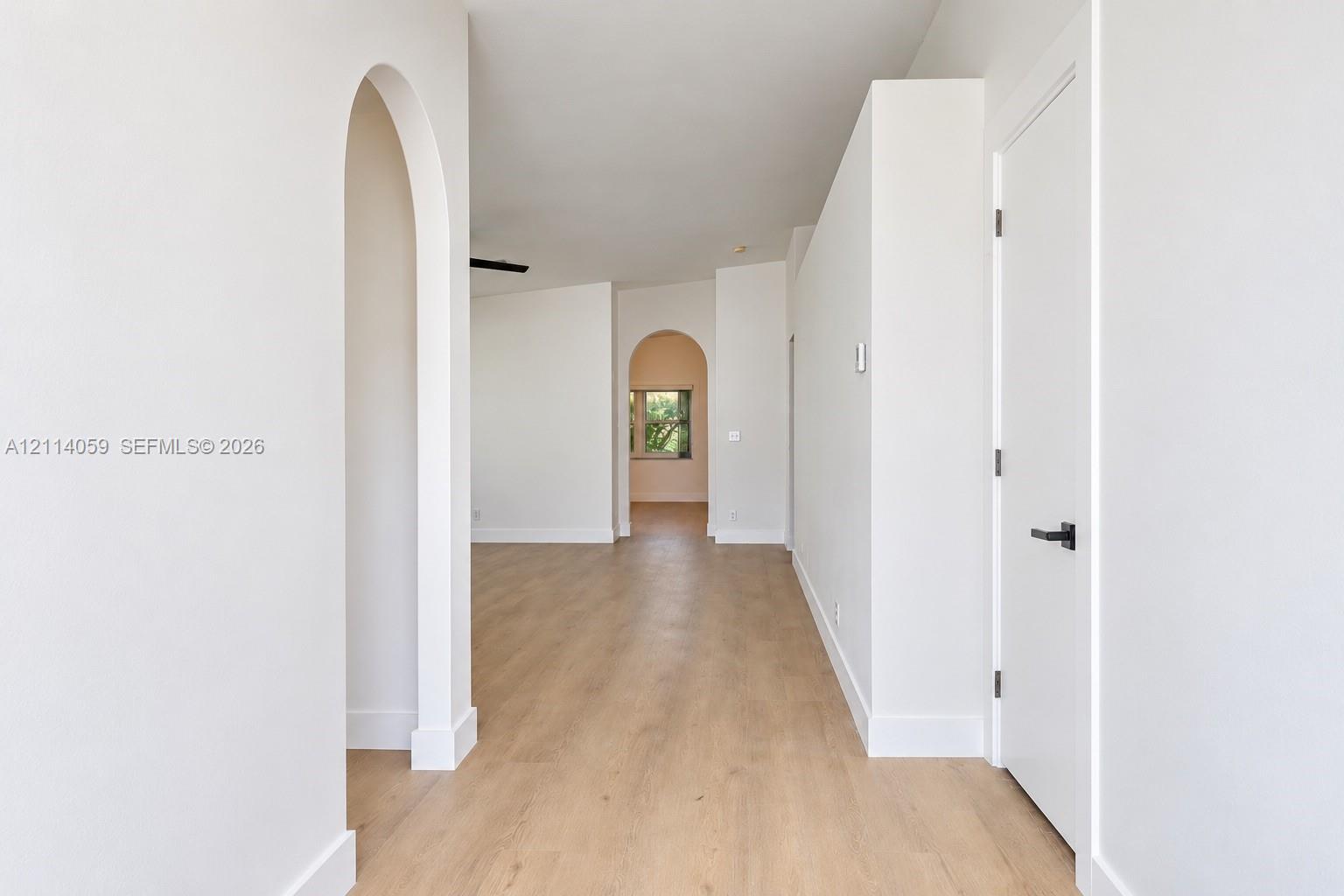 Interior space featuring arched doorways, wood-finish flooring, and minimalist white walls with matte black hardware