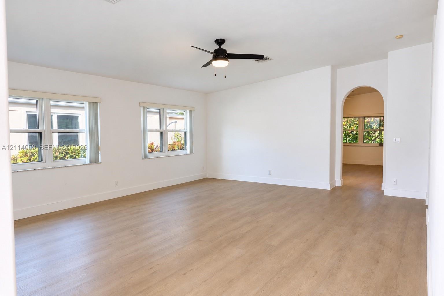 Open interior space featuring wood-finish flooring, an arched entryway, dual windows, and a ceiling fan with integrated lighting