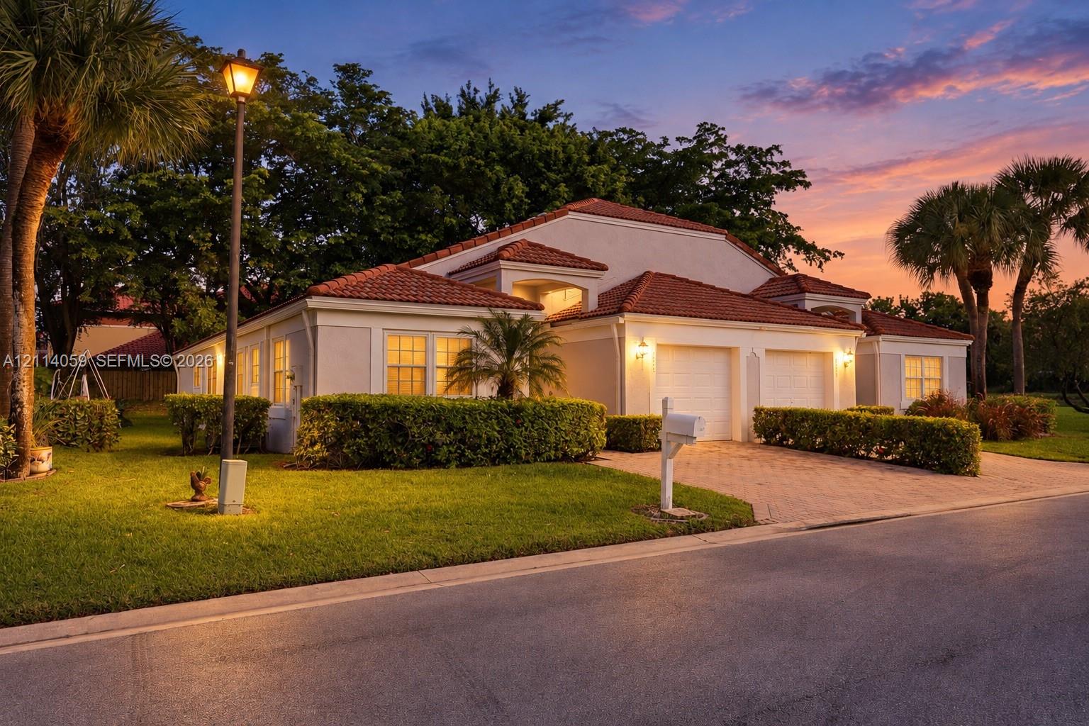 Stucco exterior featuring a multi-gabled terracotta tile roof, two-car garage, and paver driveway