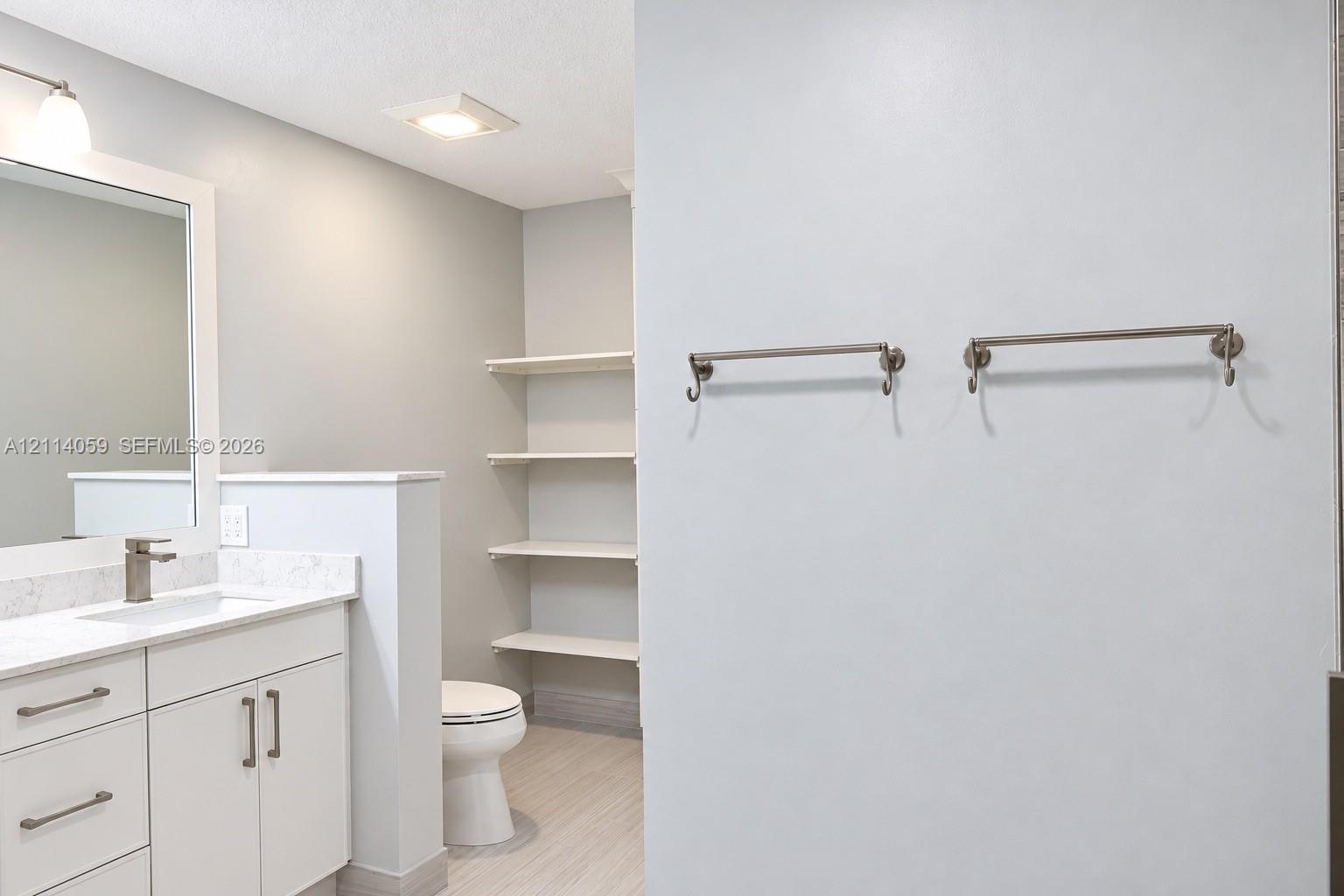 Bathroom featuring white cabinetry, stone-finish vanity countertop, undermount sink, built-in wall shelving, and dual brushed-nickel towel bars