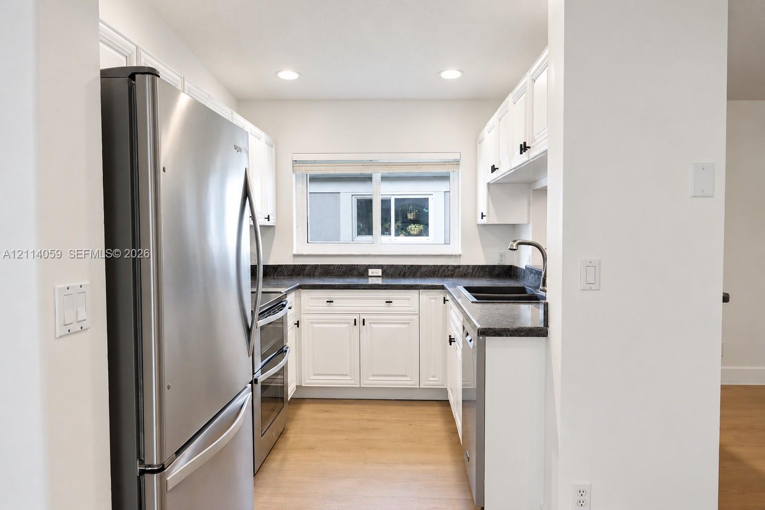 Kitchen featuring white shaker-style cabinetry, dark stone-finish countertops, stainless steel appliances, and wood-finish flooring