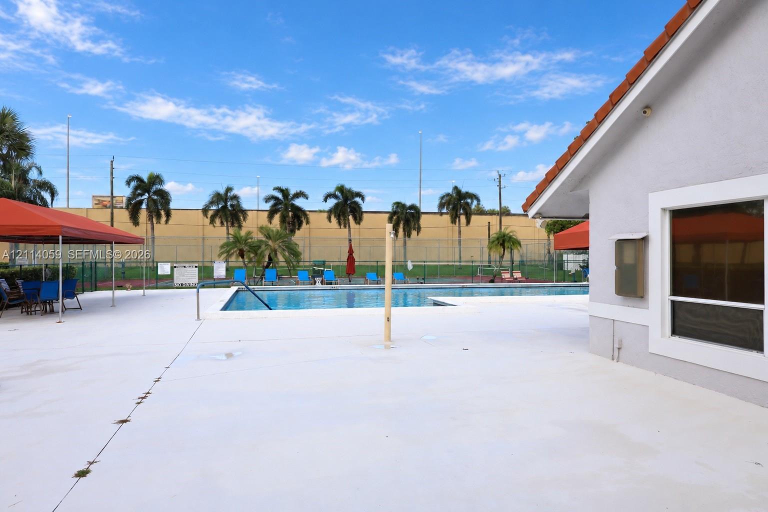 Outdoor pool area featuring a concrete deck, metal perimeter fencing, and palm tree landscaping
