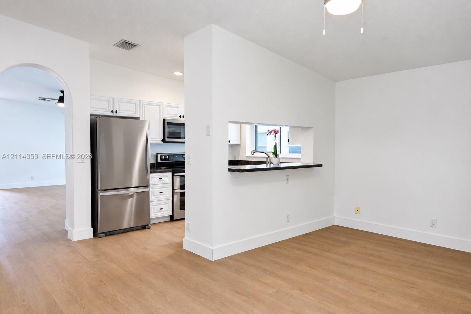 Kitchen featuring stainless steel appliances, white cabinetry, dark stone-finish countertops, and wood-finish flooring, complemented by an arched doorway