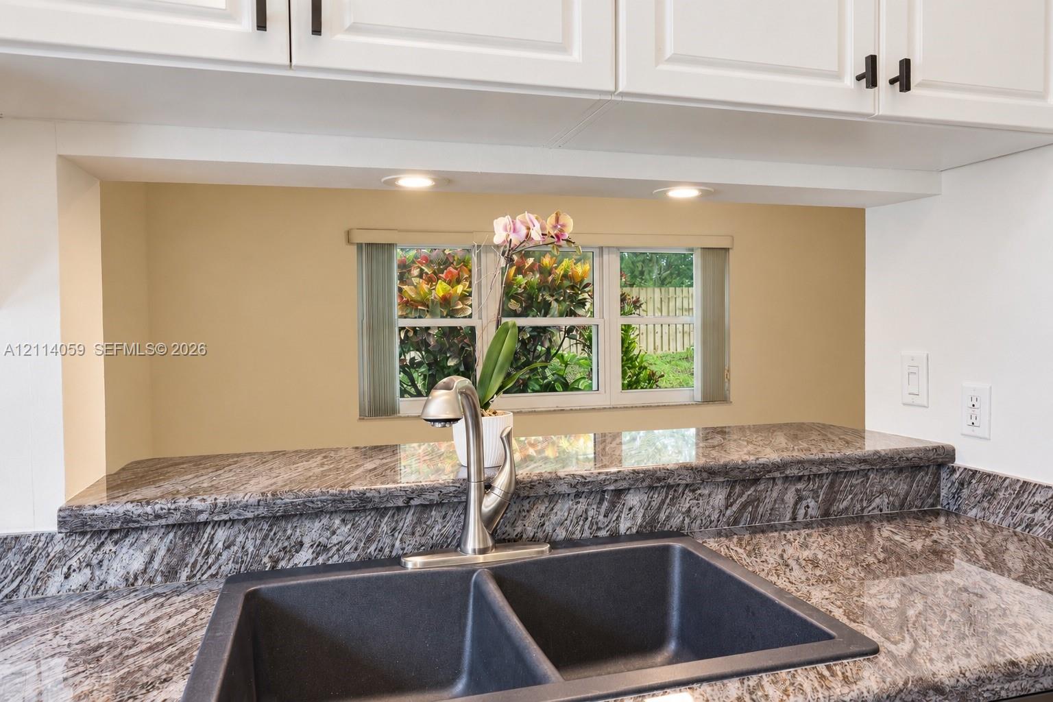 Kitchen featuring stone-finish countertops, undermount double-basin sink, high-arch faucet, white cabinetry with matte black hardware, and recessed lighting