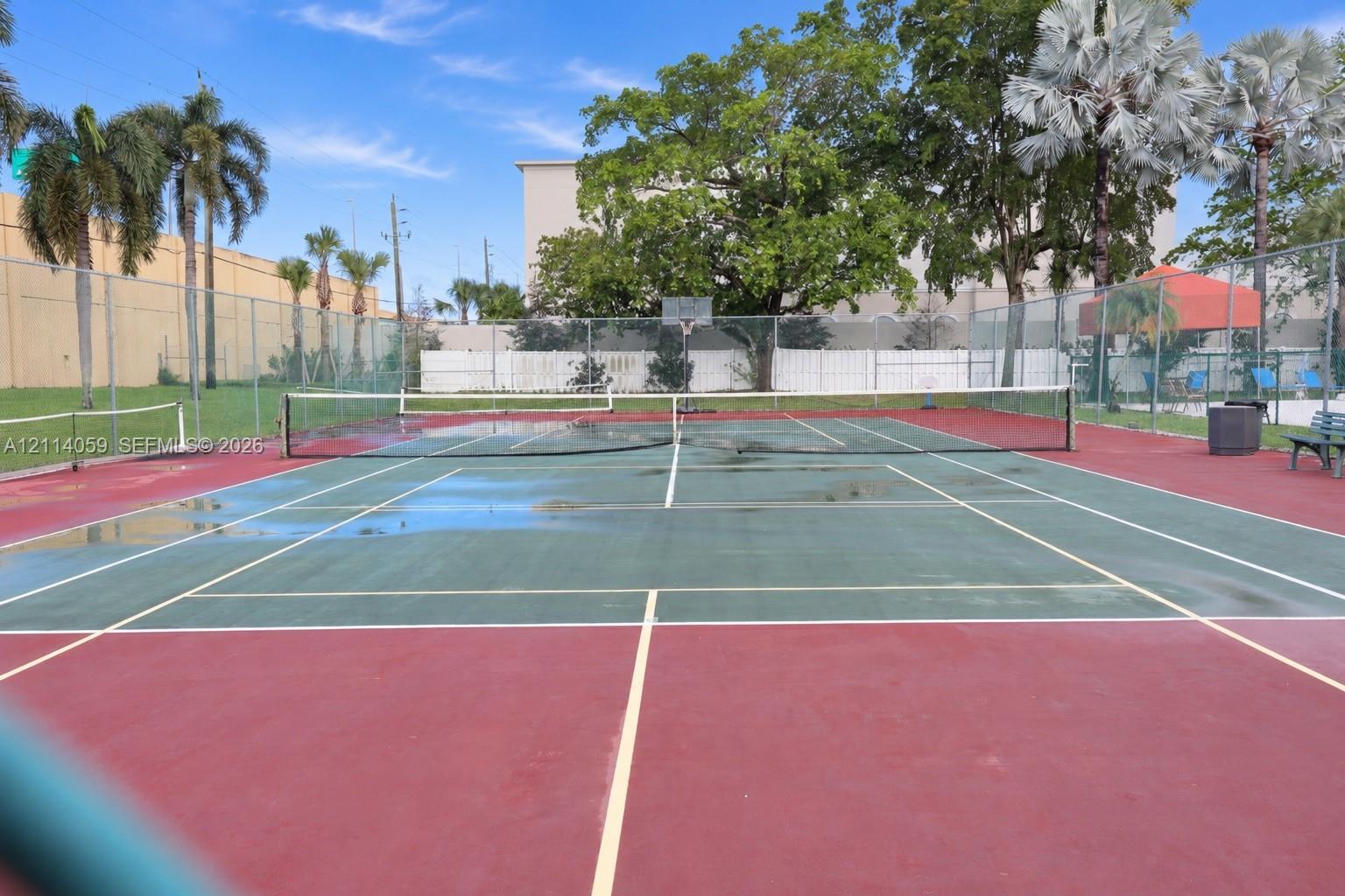 Tennis court with perimeter chain-link fencing, dual-tone hard surfacing, and integrated basketball goal