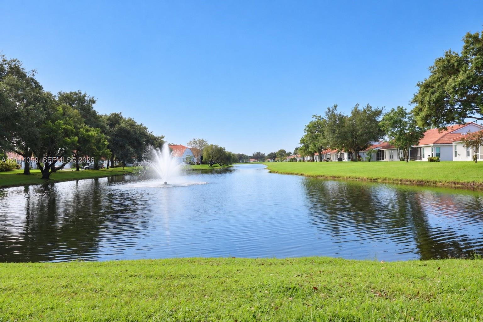 Waterfront setting featuring a central fountain, manicured lawn, and mature canopy trees