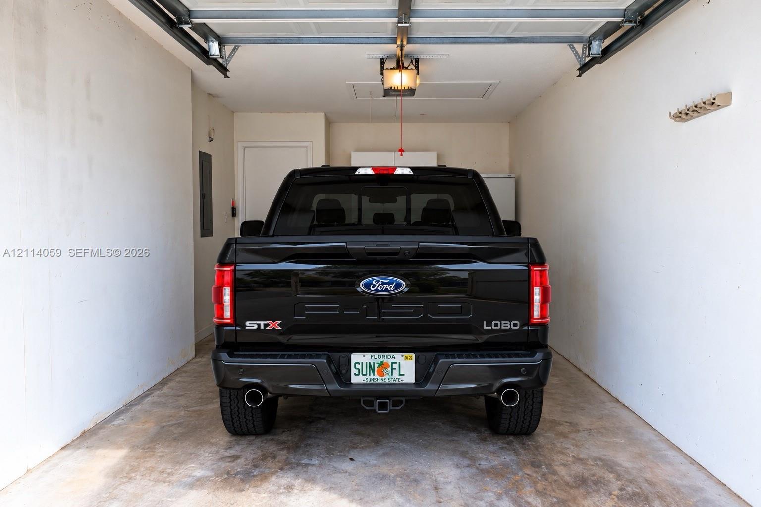 Enclosed garage featuring concrete flooring, a motorized overhead door system, ceiling-mounted light fixture, and interior access door