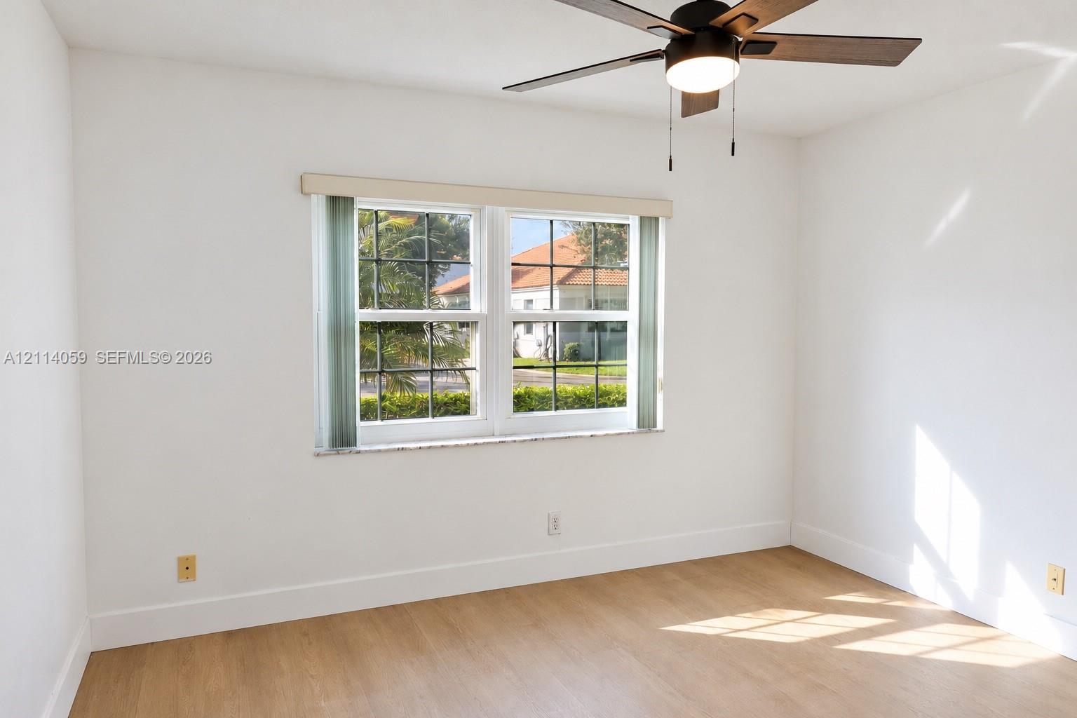 Room interior featuring wood-finish flooring, white walls, dual-pane windows with muntins, and a ceiling fan with integrated lighting