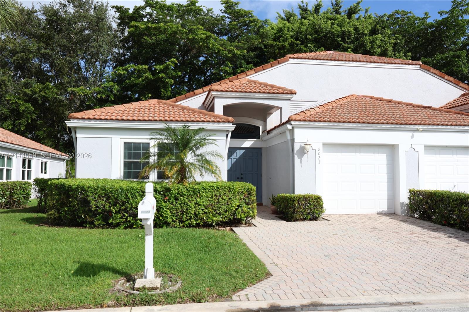 Single-story exterior featuring a terracotta tile roof, paver driveway, recessed entry, and manicured shrubbery