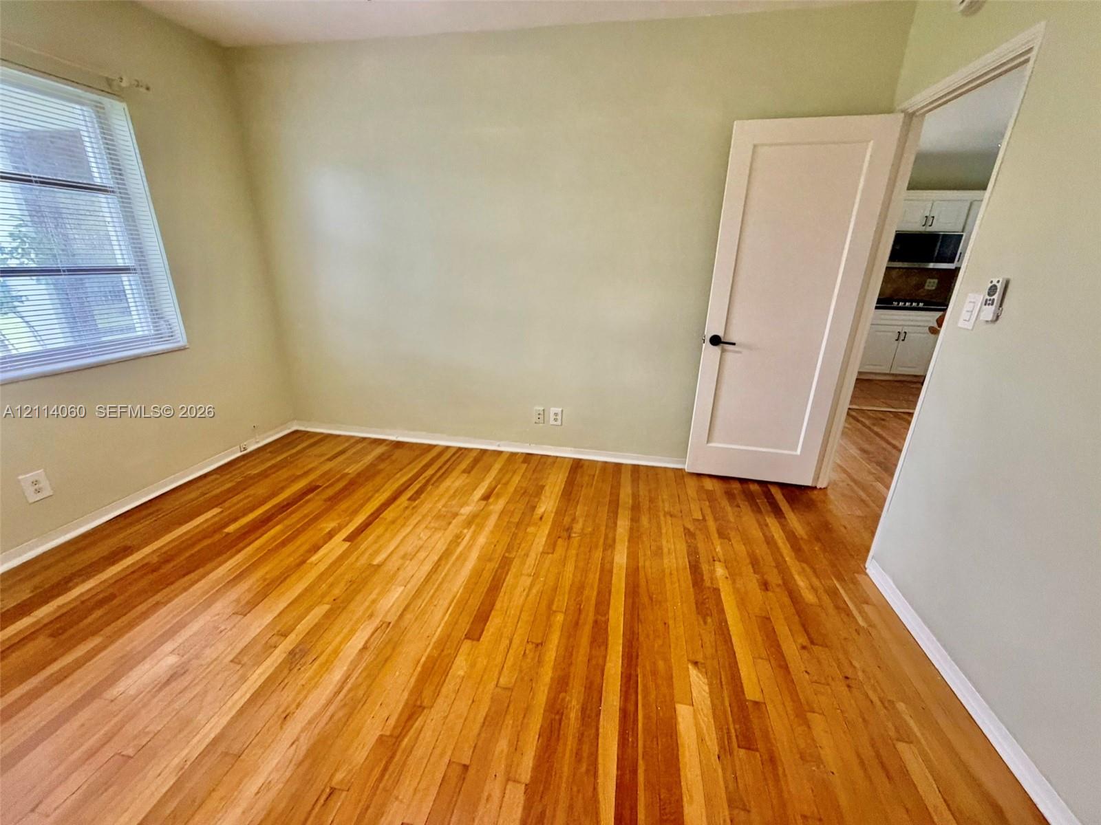Room featuring wood-finish flooring, a single-panel interior door, and a window with horizontal blinds