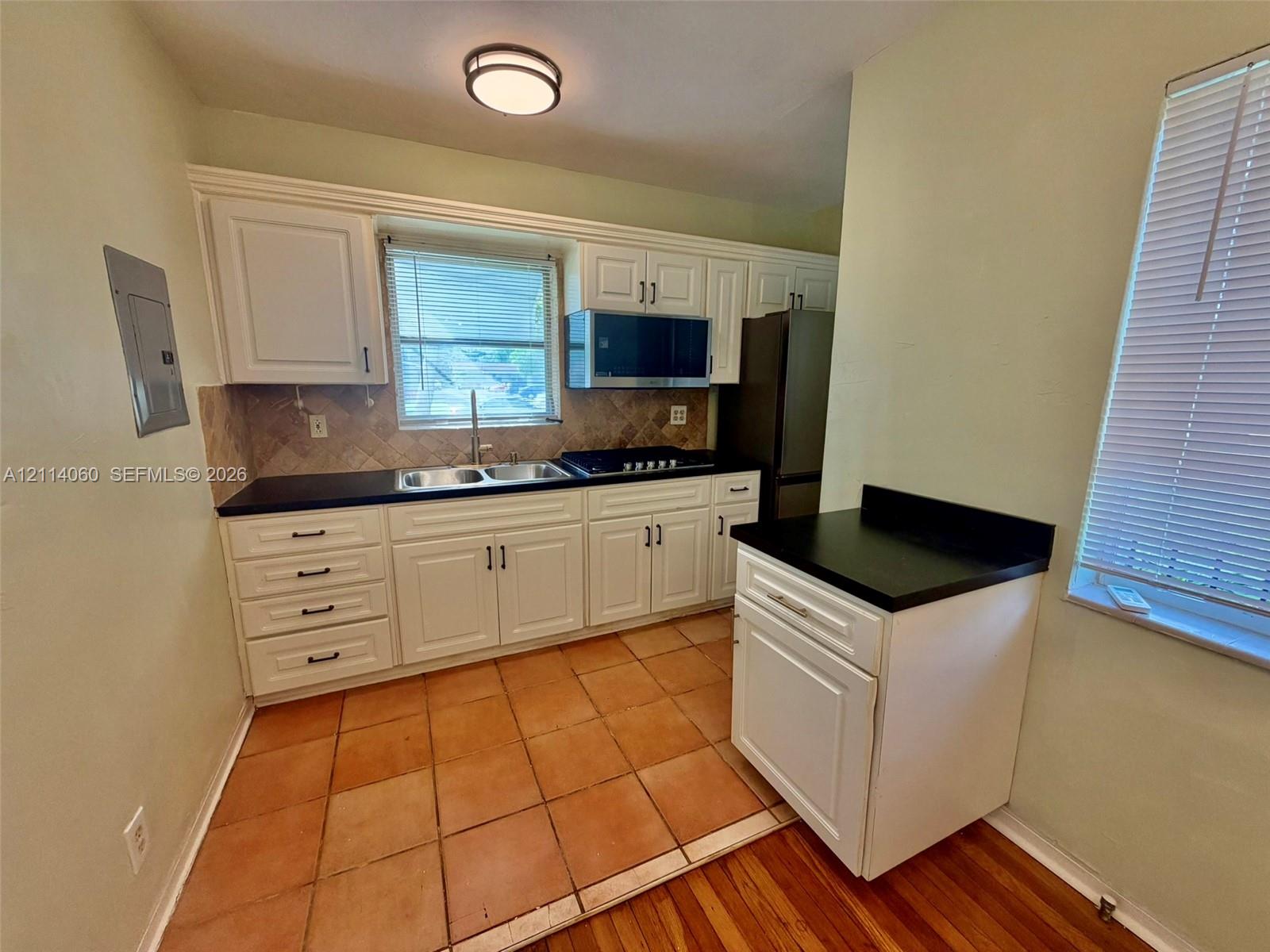 Kitchen featuring white cabinetry, dark stone-finish countertops, ceramic tile backsplash, built-in microwave, and terracotta-style floor tiles