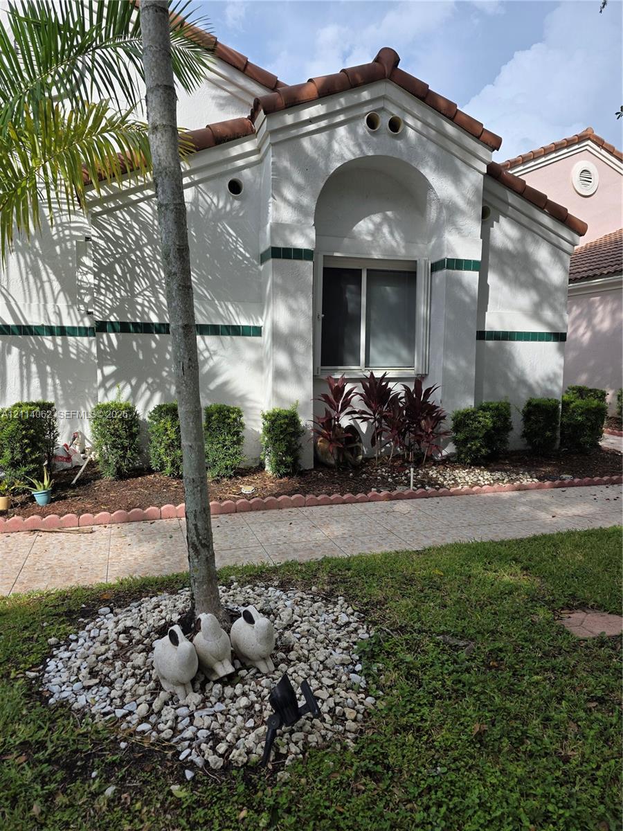 Stucco exterior featuring arched architectural detailing, decorative tile accents, and a tile roof, complemented by a paved walkway and mature landscaping